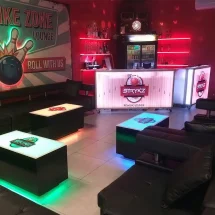 Bowling alley lounge setup featuring two custom branded portable bars on casters with white LED lighting and bowling alley graphics, surrounded by matching LED lighted cubix cocktail tables.