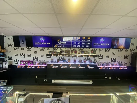 Wall-mounted LED retail shelves at Higharchy dispensary featuring custom illuminated text "Queens Candy" and "Kings Chronic" holding glass jars of cannabis.